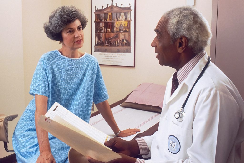 A patient sitting in a doctor's office with a medical professional discussing test results from a liquid biopsy